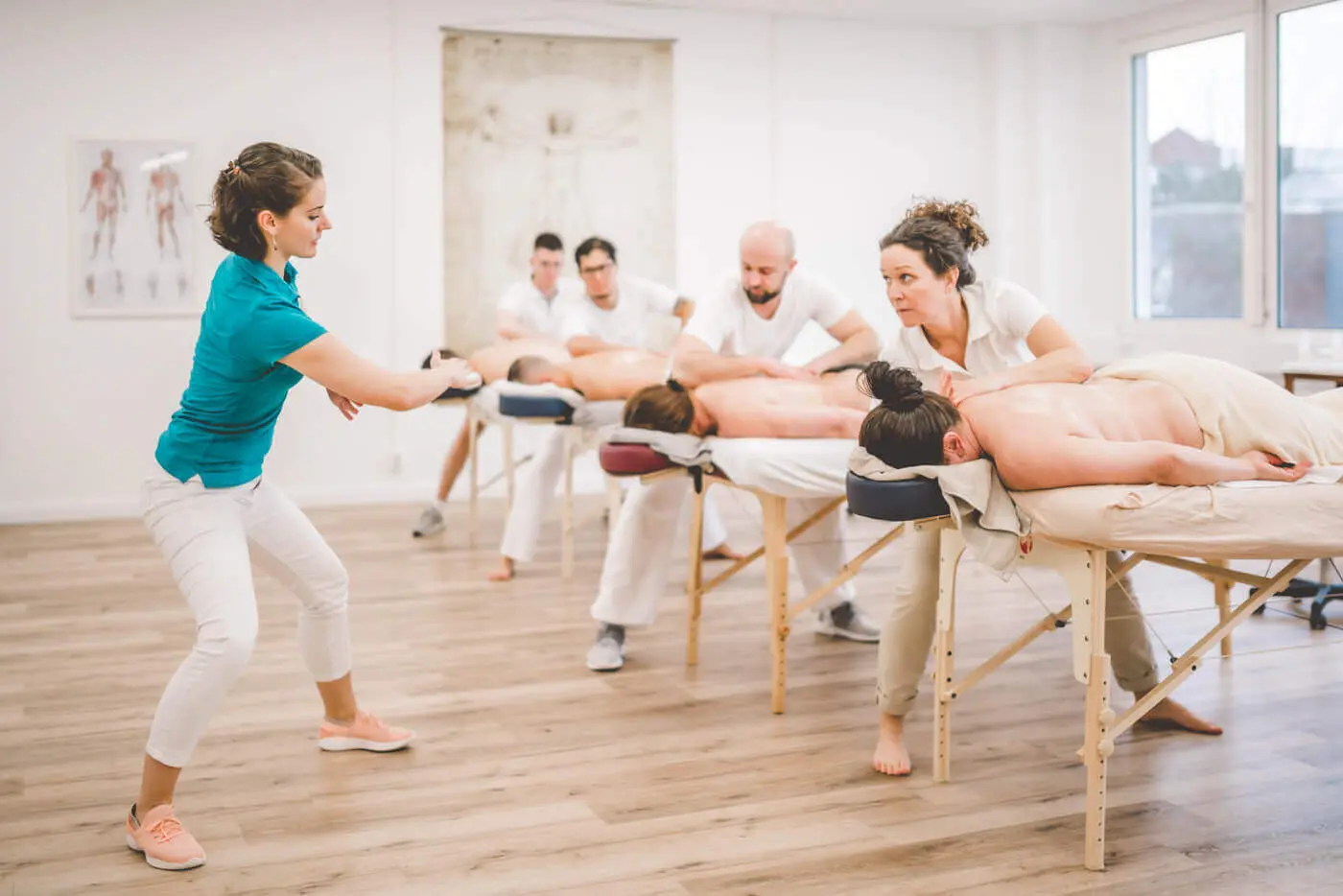 Dozentin korrigiert die Handhaltung mehrerer Teilnehmender an Massageliegen